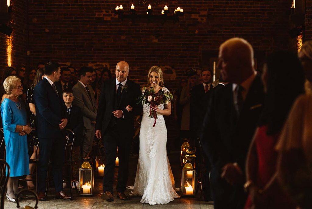 A bride walking down the aisle with her father, lanterns lining the way