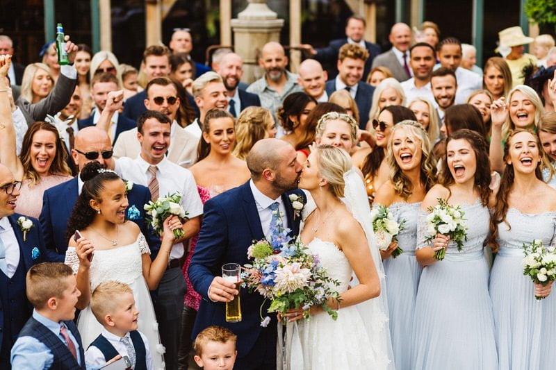 Guests packed in around a couple kissing, everyone cheering