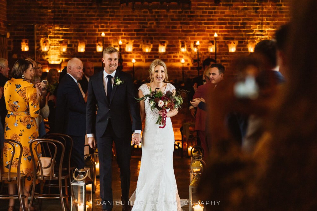 A couple at the top of the aisle in the ceremony room at Hazel Gap, candlelit brick wall behind them