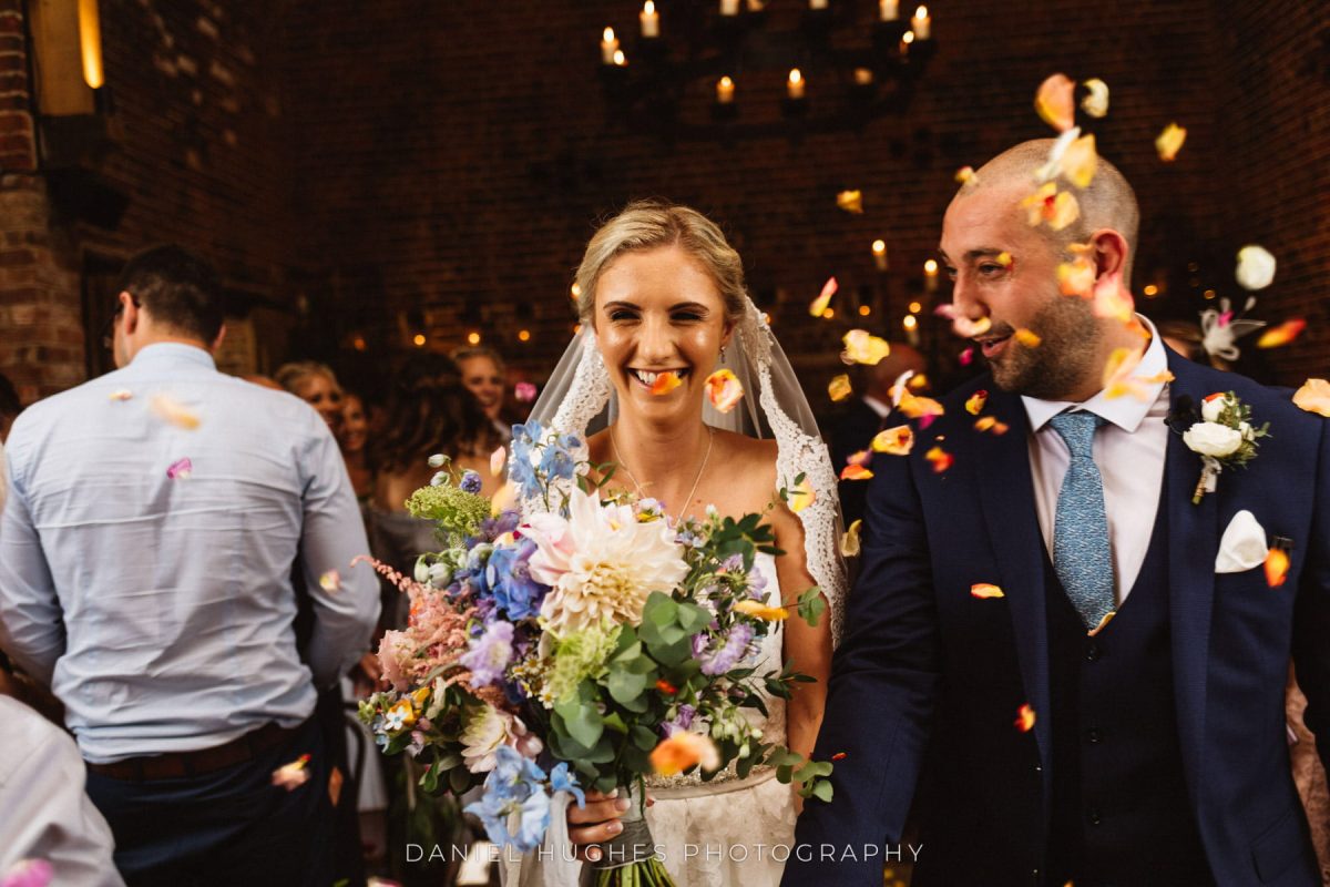 Smiling bride and groom walking up the aisle with confetti.