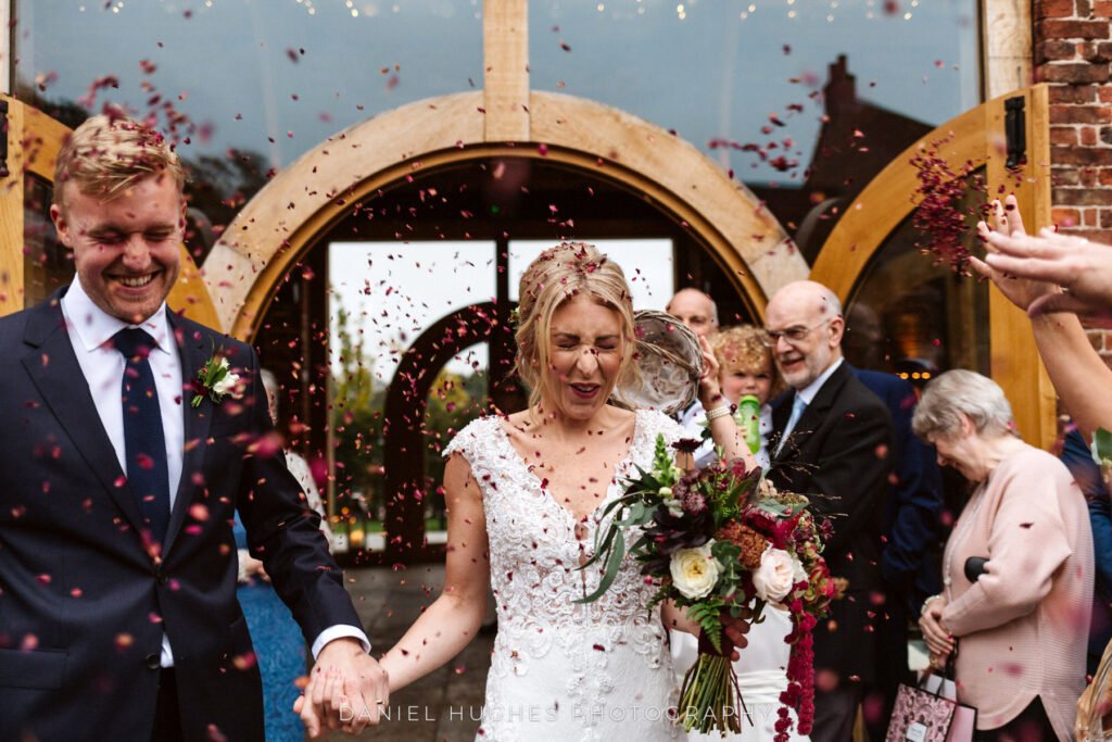 A couple walking out through the arched doorway into a shower of red confetti