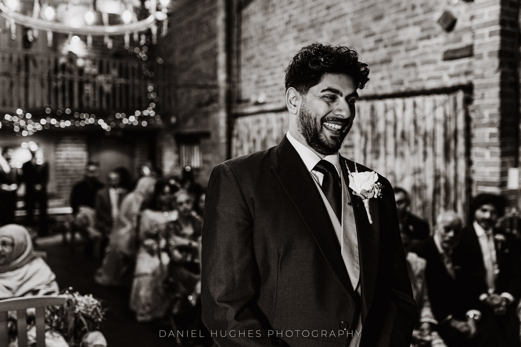 Black and White image of Gurpreet smiling as he waits for Kamrun to come up the Aisle in the Granary Barn.