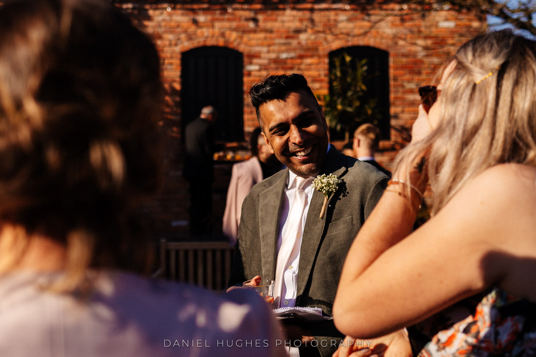 A wedding guest is smiling, with the Exposed brickwork of the Barley Barn behind him.